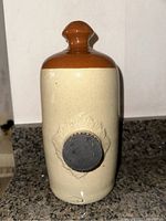 Front view of antique ceramic hot water bottle showing two-tone glaze and textured stopper.