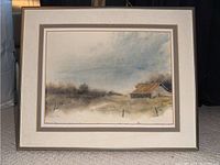 Framed watercolor painting showing a rural barn landscape with muted colors and cloudy sky.