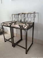 Front view of two metal bar stools with patterned cushioned seats detached from frames.