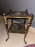 Full side angle view showing the whole brass end table with two tiers, decorative legs and claw feet on a carpeted surface.