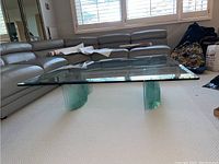 Full view of the glass coffee table showing the clear glass top and the curved glass base with a wave-like structure.