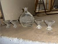 Full set of crystal decanter and four small glasses displayed on a stone surface.