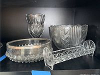 Photo showing crystal vase, glass bowl with silver-like trim, cracker tray, and another glass bowl on a shelf