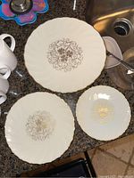 Top view of three different sized plates showing white surface with gold ornate filigree designs and gold rim detailing.