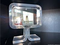 Front view of clear Lucite mantle clock showing the hollow rectangular body with clock mechanism inside and U-shaped base stand.