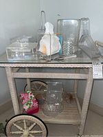 Photo showing a variety of clear Lucite-style homeware including an ice bucket, tongs, napkin holders, pitcher, clothes hanger, cheese utensils, organizer, paper towel holder, and coasters on a wicker shelf unit.