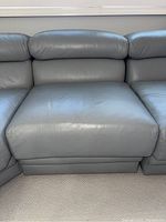 Front view of the modular sectional sofa section showing gray leather upholstery, plush padded backrest, and cushioned seating area.
