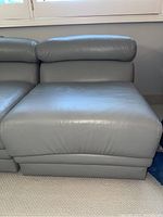 Side view of light gray leather sectional sofa piece with smooth leather cushions and padded adjustable headrest.