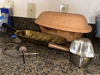 Overview of Romertopf clay pot, brass and stainless steel serving dishes, and temperature probe photographed on kitchen counter.