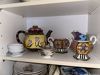 Shelf with colorful hand painted teapot, matching sugar bowl and creamer, small white tea bag holder plates, and Precious Moments dish below