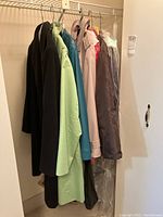 Photo showing six hanging coats of various colors and fabrics including black, green, teal, pink, and grey.