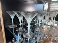 Photo showing nine vintage martini glasses with frosted butterfly designs arranged on glass shelving.