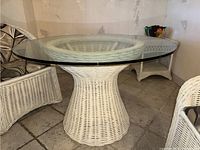 Front-side view of white wicker pedestal table with clear round glass top on tiled floor