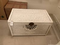 Full view of closed white wicker storage trunk with metal latch showing overall design and size.