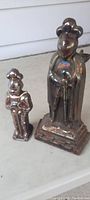 Front view of two cast iron standing figures with glazed finish, showing size comparison and detail.