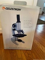 Photo of the Celestron Biological Microscope original packaging box showing specifications such as 40x, 100x, 400x power, 12mm field of view, fully coated glass optics, mirror illumination, coarse and fine focusing knobs.