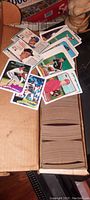 Open long cardboard box showing rows of tightly packed cards with some cards laid on top showing player portraits and team logos from the early 1980s era.