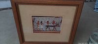 Full view of framed and matted Egyptian themed artwork under glass in solid wood frame, showing the entire piece and frame.