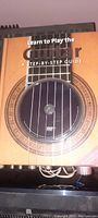 Front cover of the instructional guitar book showing a guitar sound hole and strings, title 'Learn to Play the Guitar A Step-By-Step Guide'