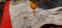 Full view of the lot showing a divided clear candy dish, a clear pedestal cake plate, an open lattice rectangular clear dish, and an amber goblet.