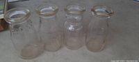 Four heavy glass antique milk bottles lined up, showing clear embossed lettering and varying shapes