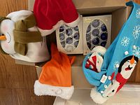 Shows assorted Christmas decorations including red and orange Santa hats, box of purple balls, and blue Christmas stockings with teams logos.