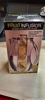 Box front view showing Fruit Infusion branding, product image of clear plastic pitcher with internal fruit infuser containing lemon slices, and usage suggestions.