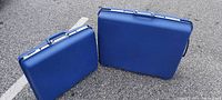 Two vintage blue Samsonite hard case suitcases, 16" and 24" sizes, shown standing upright outdoors on pavement.