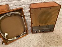 Overview of amplifier and speaker cabinets side by side on carpeted floor, cable inside speaker cabinet