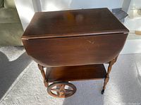 Side view of antique wooden tea cart showing drop leaf folded down and wooden wheels