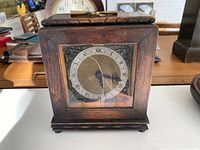 Front view of antique wooden mantle clock showing dial with Roman numerals and metal decorative corners inside glass.
