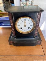 Front view of antique black mantle clock with marble columns and round white dial with Roman numerals.