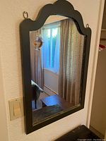 Front view of the wooden framed antique wall mirror hung on wall, showing reflective glass and shaped arched top edge.
