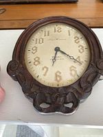Front view of antique New Haven clock showing dial, numbers, hands, and wooden frame with detailed carved designs.
