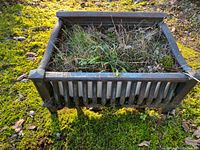 Top and front view of vintage rectangular cast metal planter with grass inside, showing vertical slats and thick cast edges.
