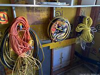 Wide view showing multiple coiled extension cords, hoses, and yellow rope hanging on wall.