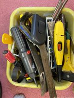 Top view of lot showing a variety of hand tools including screwdrivers, files, a claw hammer, utility knife, and tape measure case in a yellow bin.
