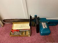 Makita electric chainsaw with chain bar and original tool kit in box with instruction sheet beneath chainsaw bar.