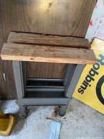 Side view showing wood top and gray metal folding legs of one saw horse.