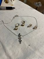 Photo showing two pairs of pearl earrings and one diamond pendant necklace with chain laid out on a white fabric surface.