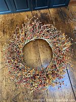 Photo showing an autumnal wreath with twigs and various small orange berry decorations on a wooden surface.