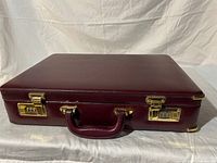 Closed maroon briefcase resting on a white cloth background, showing the closed top and handle.