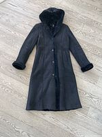 Full front view of black sheepskin coat with hood and button-front closure on wood floor