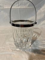 Front view of lead crystal ice bucket featuring vertical fluted cuts, silver plate rim and handle.