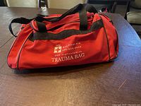 Photo of the red trauma bag with black handles labeled 'DCF First Aid Trauma Bag'.
