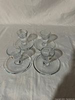 Four clear glass egg cups with attached saucers arranged on a cloth backdrop showing overall look and quantity.