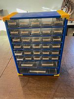 Front view showing 33 clear plastic drawers arranged in rows within a blue metal cabinet with yellow corner protectors.