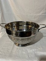 Side perspective of large stainless steel colander showing perforated sides, shiny finish and handles.
