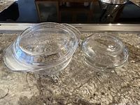 Two lidded glass casserole dishes side by side on a granite countertop, showing overall size difference and clear glass material.