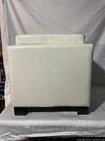 Side view of off-white faux leather ottoman showing clean exterior upholstery and wooden legs.